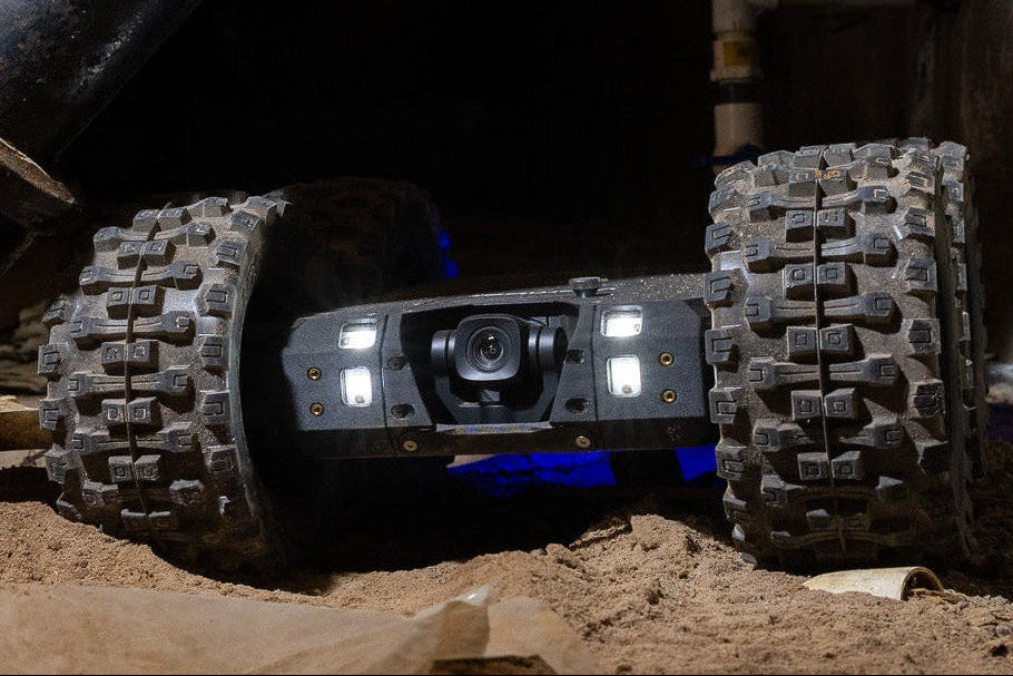 Robotic device with wheels navigating through a dark, industrial setting with pipes.